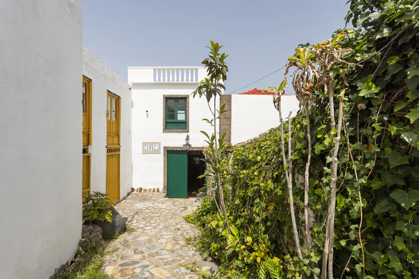 Exterior view of a white building with green door and window, stone path, and ivy-covered wall.