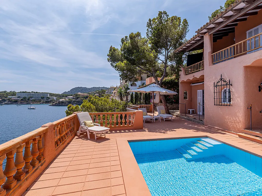 Luxury villa with pool overlooking the ocean. Terracotta patio with lounge chairs and a white umbrella.