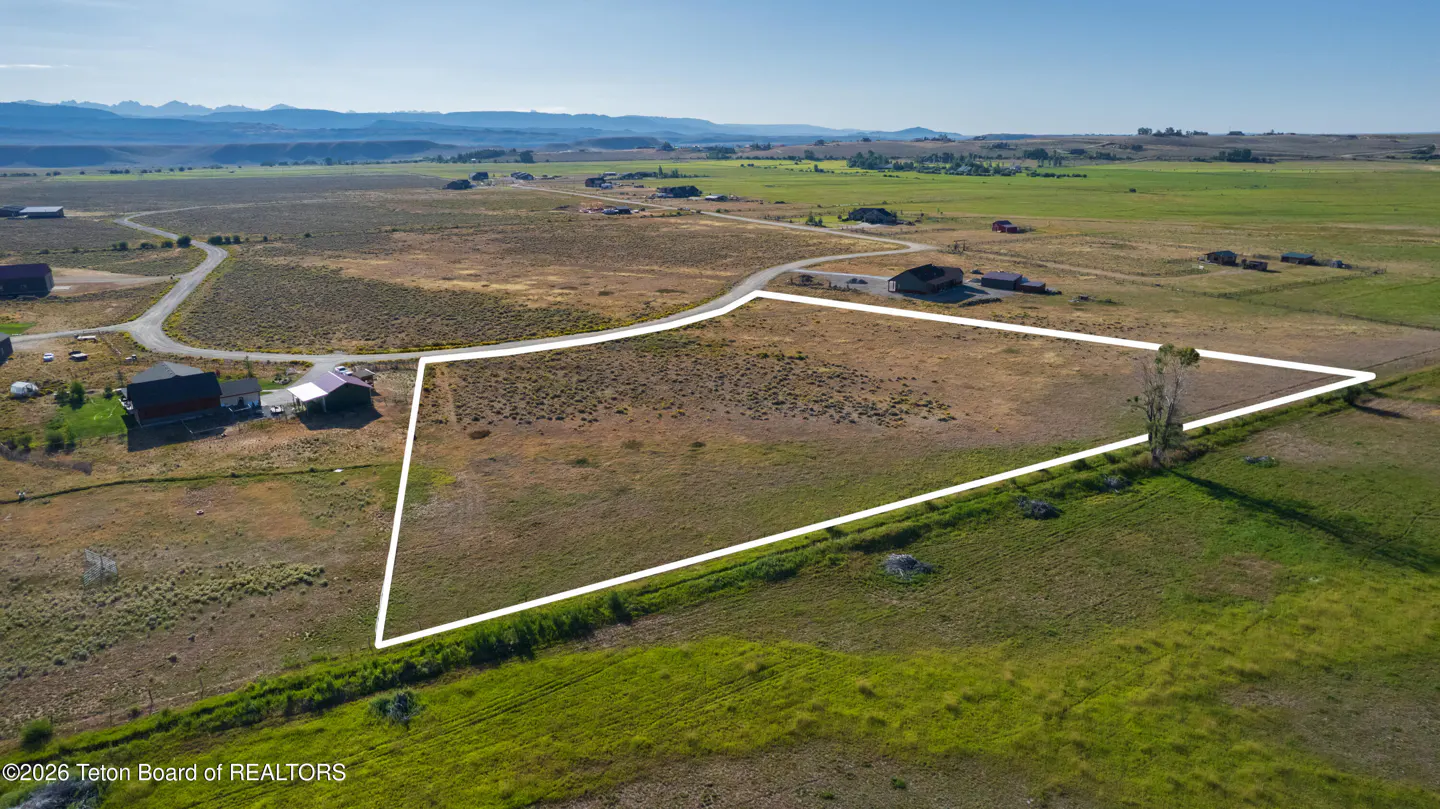 Aerial view of a vacant lot outlined in white, with green fields and mountains in the background.