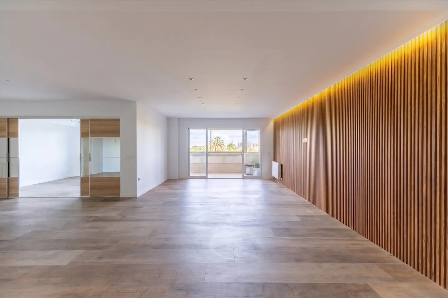 Bright, empty room with wood floors, white walls, and a wood slat accent wall with a balcony view.