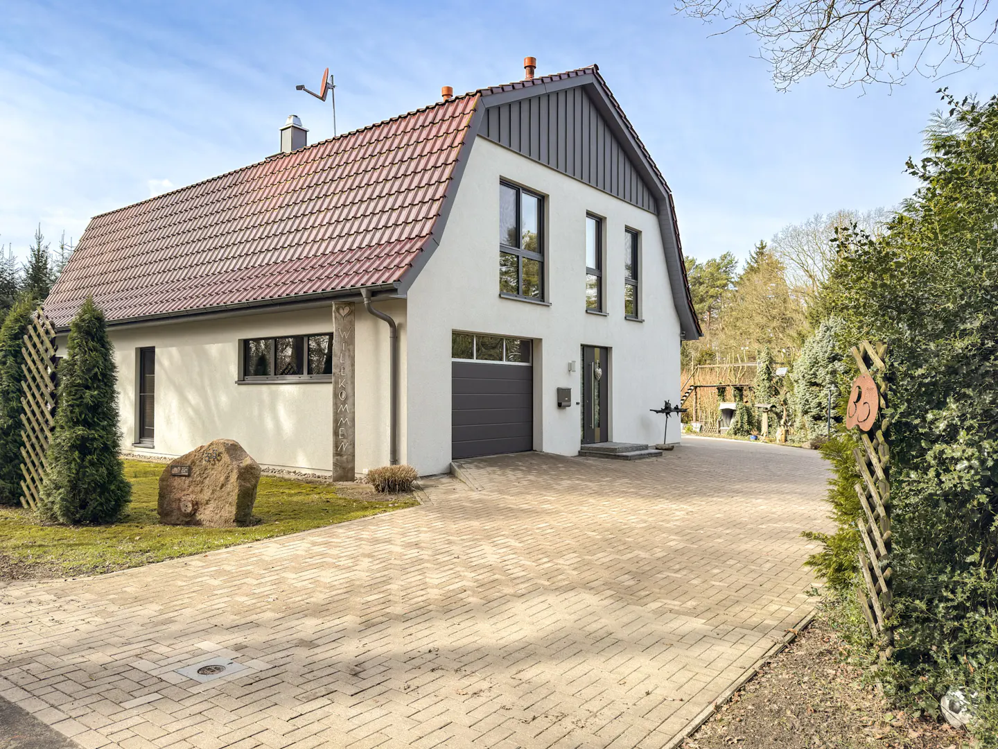 Two-story white house with a red tile roof and gray trim, a gray garage door, and a brick driveway.