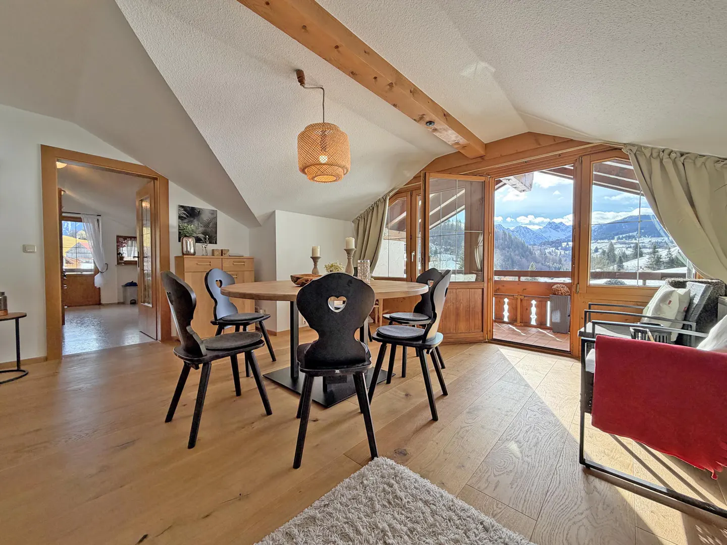 Attic dining area with wood floors, round table, black chairs with heart cutouts, and mountain view from the balcony.