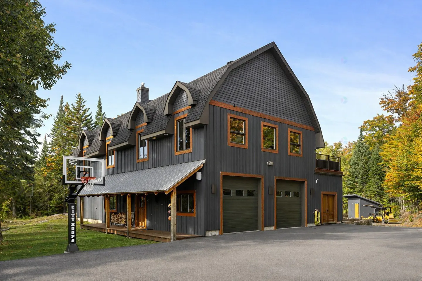 Two-story gray house with a gambrel roof, brown trim, and a porch. A basketball hoop stands in the front yard.