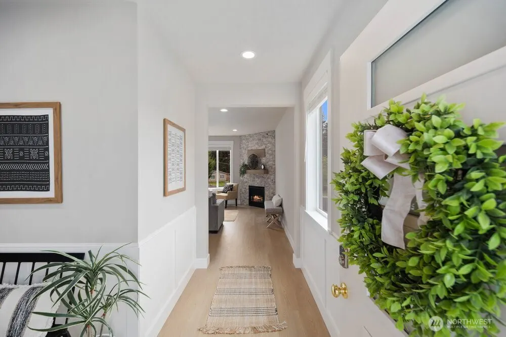 Hallway view into a living room with a fireplace. A green wreath hangs on the white front door. Artwork adorns the light gray walls.