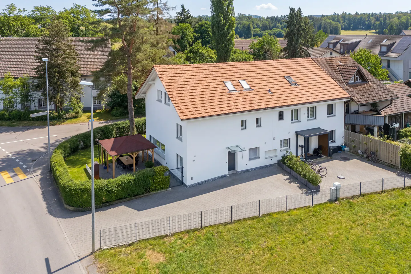 Aerial view of a white two-story house with a red tile roof, a gazebo, and a green lawn.