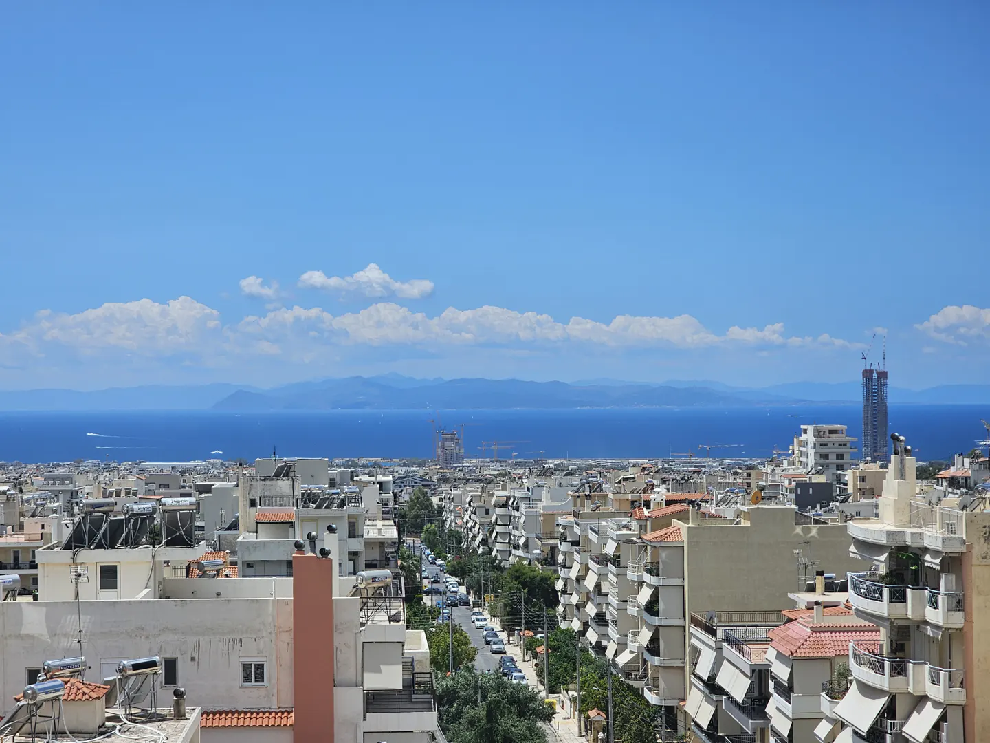 Elevated view of a dense Mediterranean city with white buildings, solar panels, and a distant blue sea under a clear sky.