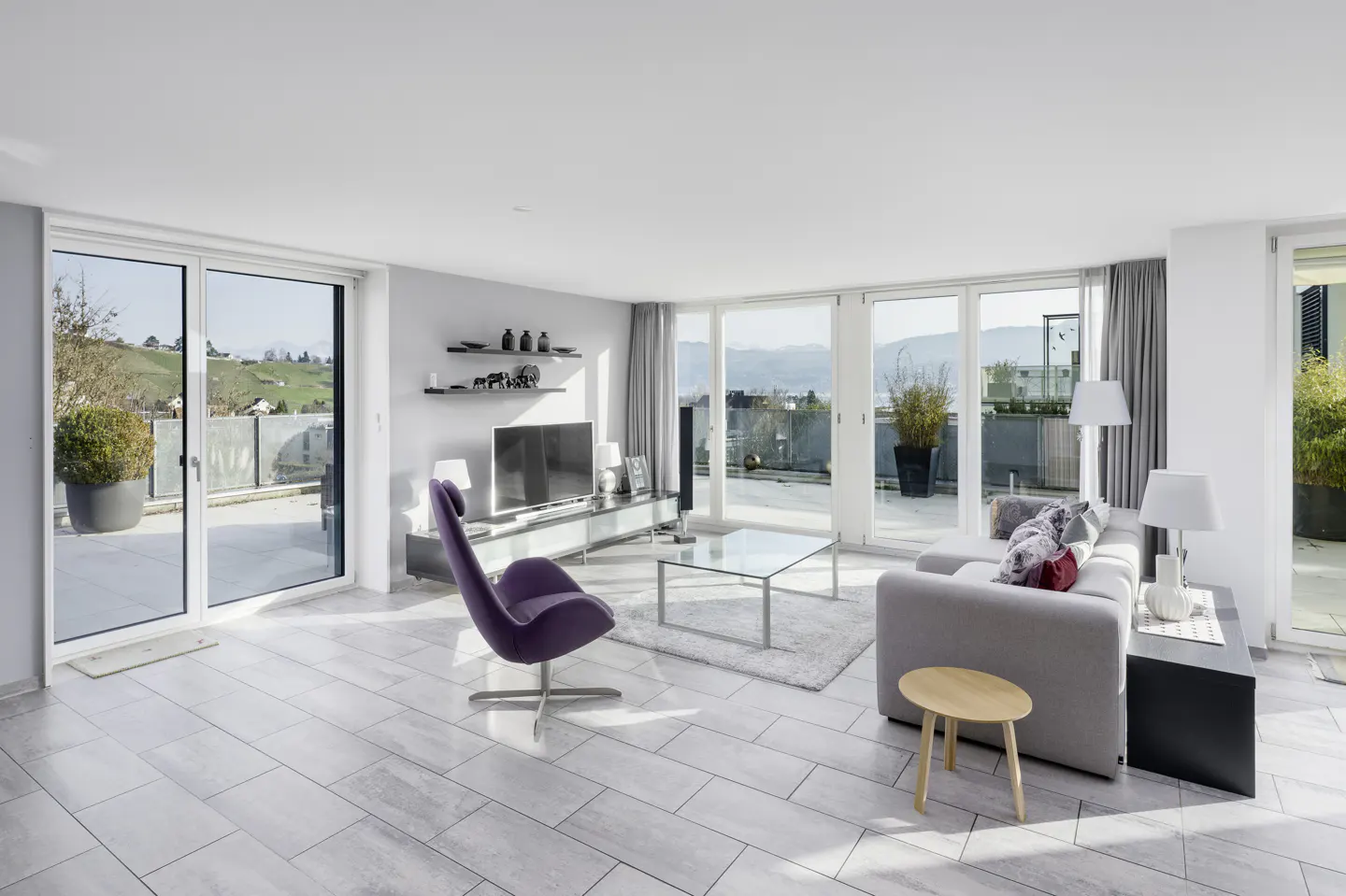 Bright, modern living room with gray tile floors, sofa, purple chair, and sliding glass doors to a balcony with a view.