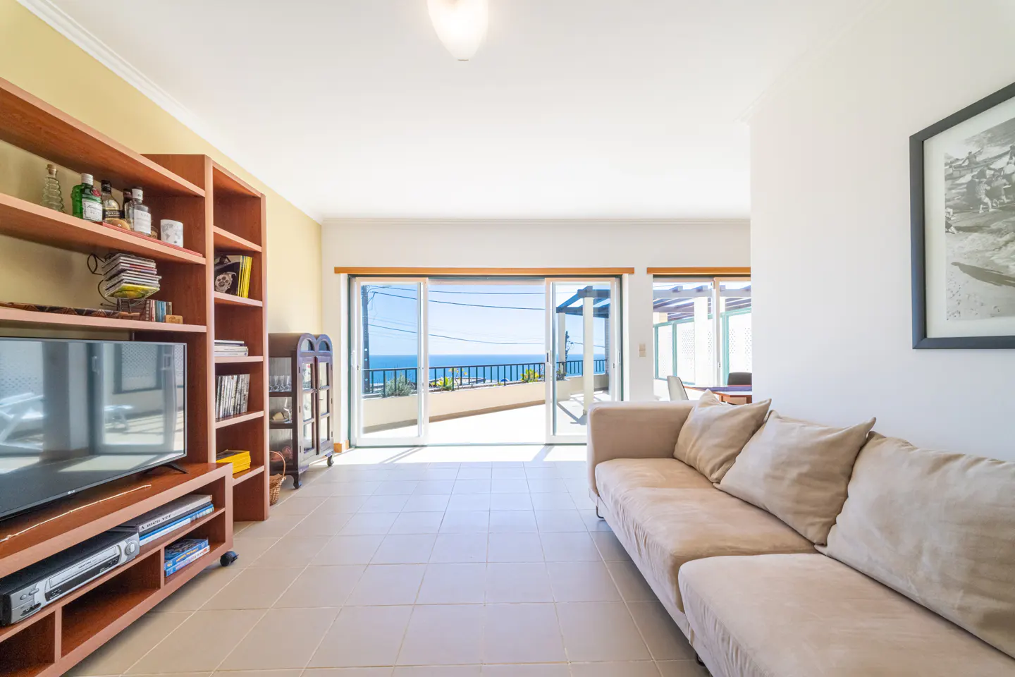 Living room with beige sofa, wood shelves, and ocean view through sliding glass doors.