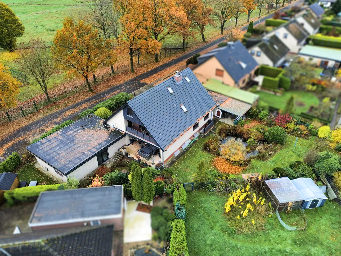 Aerial view of a house with a blue roof, surrounded by trees with autumn foliage and green lawns.