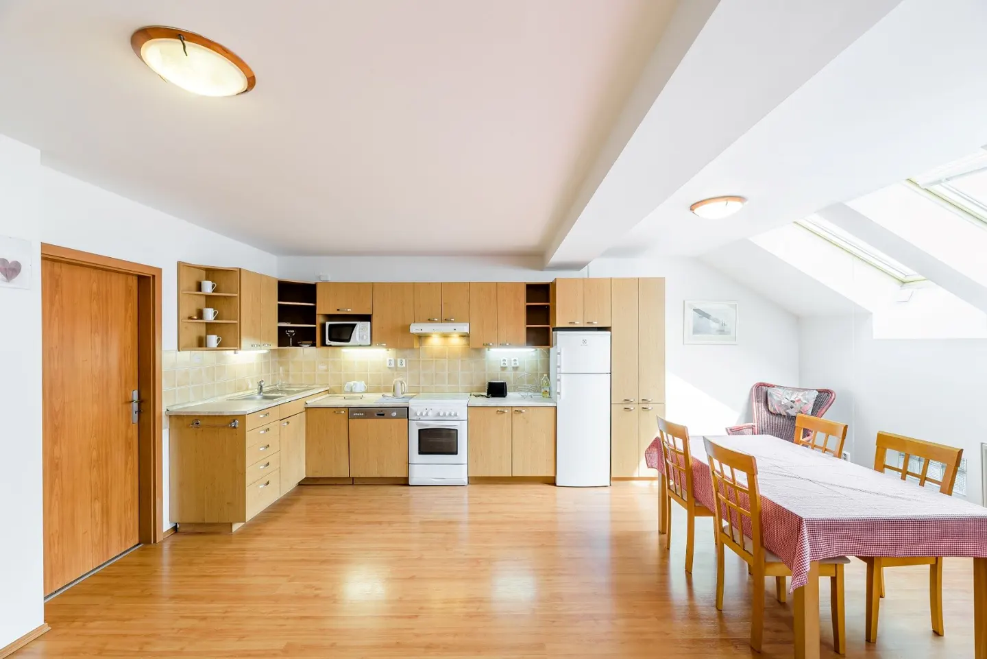 Bright kitchen with light wood cabinets, white appliances, and a dining table with chairs under a sloped skylight ceiling.