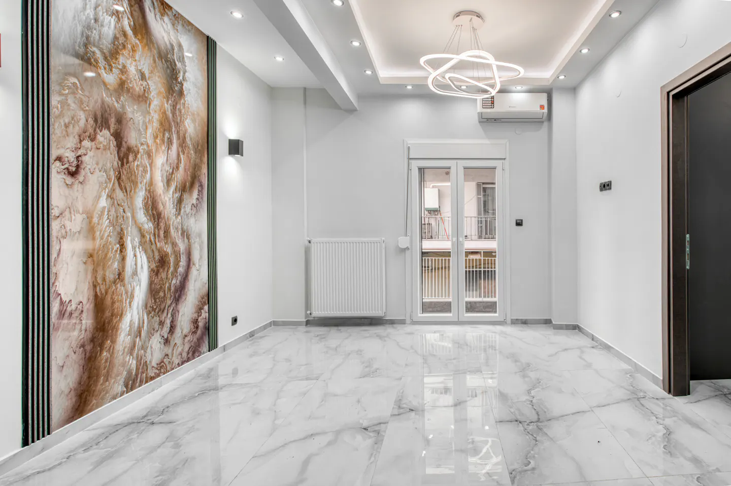 A modern, empty room with white walls, marble floors, and a decorative wall panel. A white radiator and a glass door are visible.