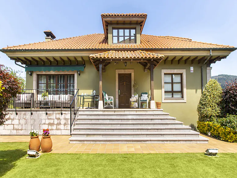 Exterior view of a two-story house with a red tile roof, olive green walls, and a large stone staircase leading to the front door.