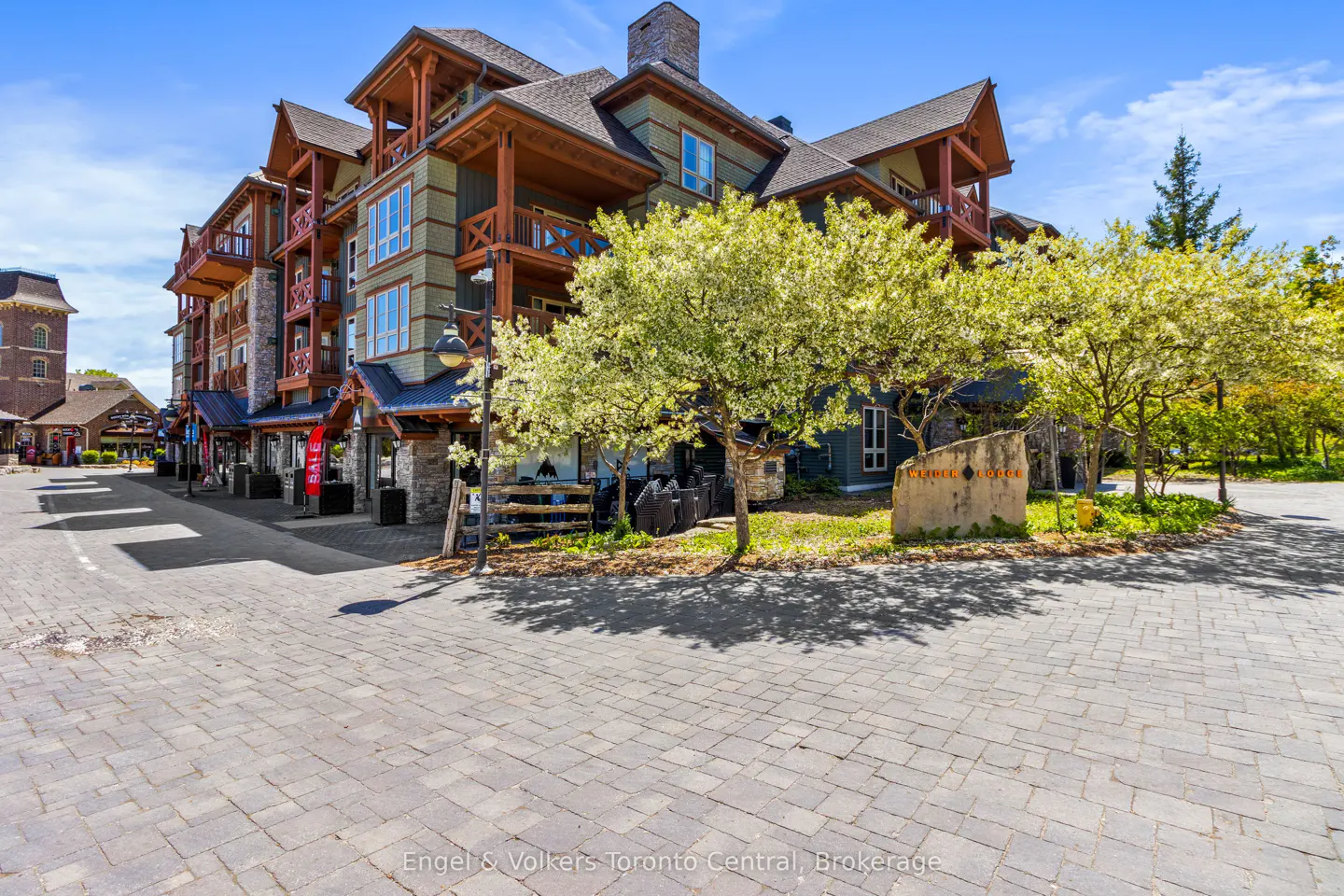 Exterior view of a multi-story building with wood balconies and green siding, set on a cobblestone street with trees.