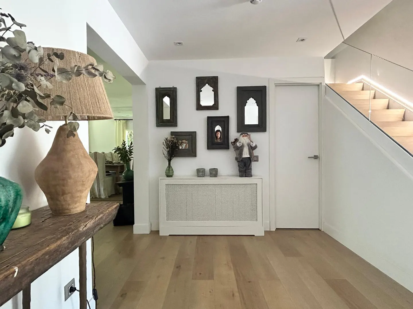 Modern hallway with light wood floors, a white radiator cover, gallery wall of mirrors, and a rustic table with a lamp.