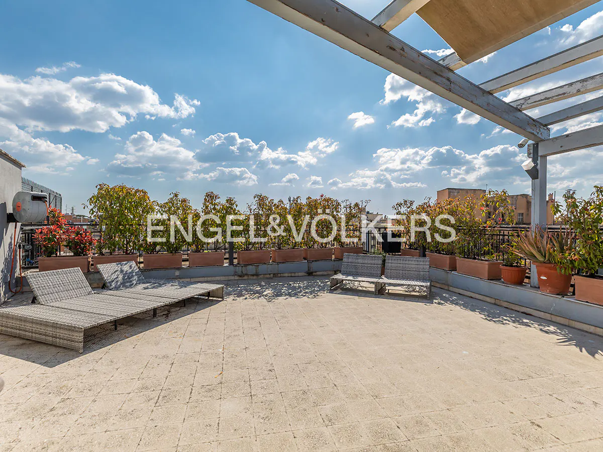 Rooftop terrace with lounge chairs, benches, and potted plants. The Engel & Völkers logo is superimposed on the image. Blue sky with clouds.