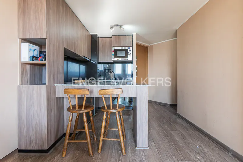 A kitchen with wood cabinets, a marble countertop, and two wooden bar stools.