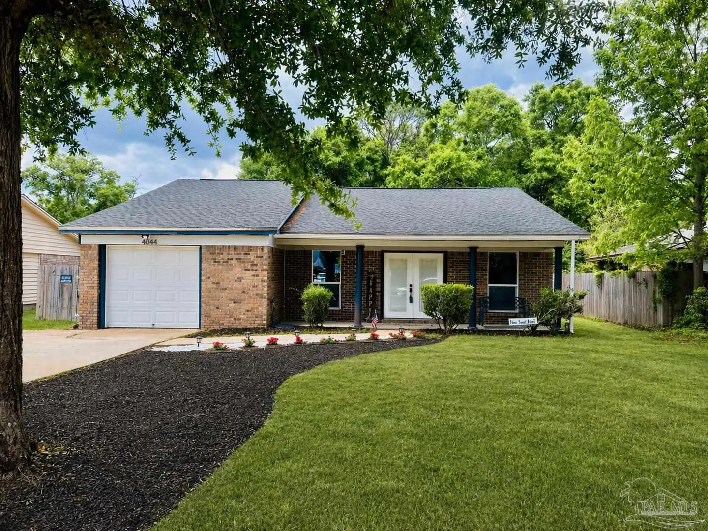 A single-story brick house with a white garage door, a gray roof, and a green lawn.