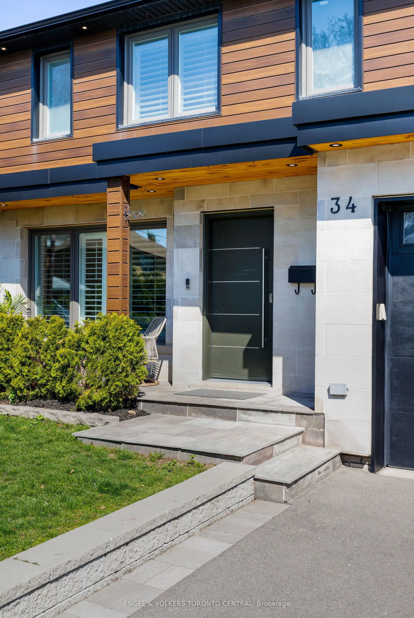 Modern two-story house with wood and stone exterior. A dark green front door with a silver handle is visible. The house number "34" is on the right.