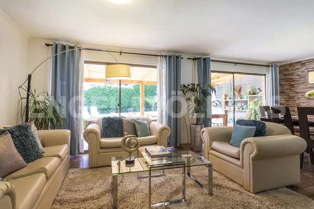Bright living room with cream sofas, blue accent pillows, glass coffee tables, and large windows with blue curtains.