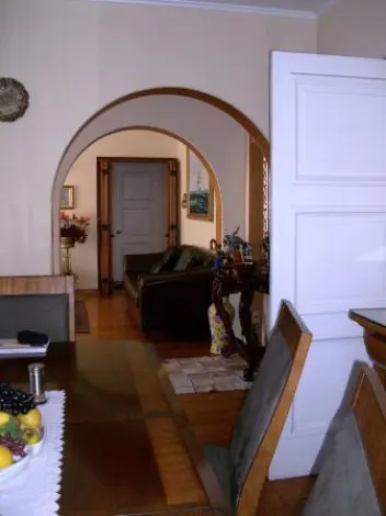 Interior view of a home with arched doorways leading to a living room with a brown leather sofa. A dining table and chairs are in the foreground.