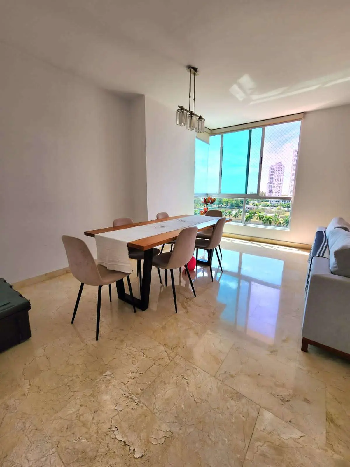 Bright, modern dining area with a long wooden table, six chairs, and a large window with a city view.