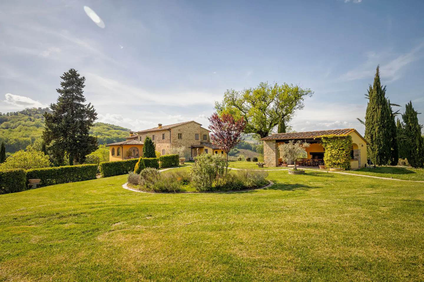 Exterior view of a Tuscan-style villa with a large green lawn, trees, and a covered patio.