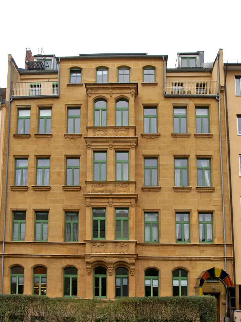 A tan apartment building with green window frames and a colorful archway entrance.