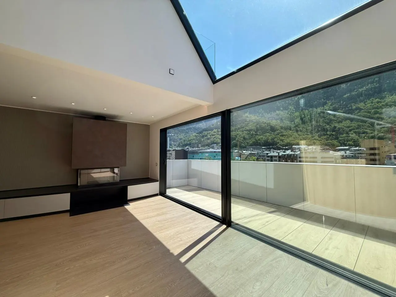 Bright, modern living room with a fireplace, light wood floors, and large sliding glass doors to a balcony with mountain views.
