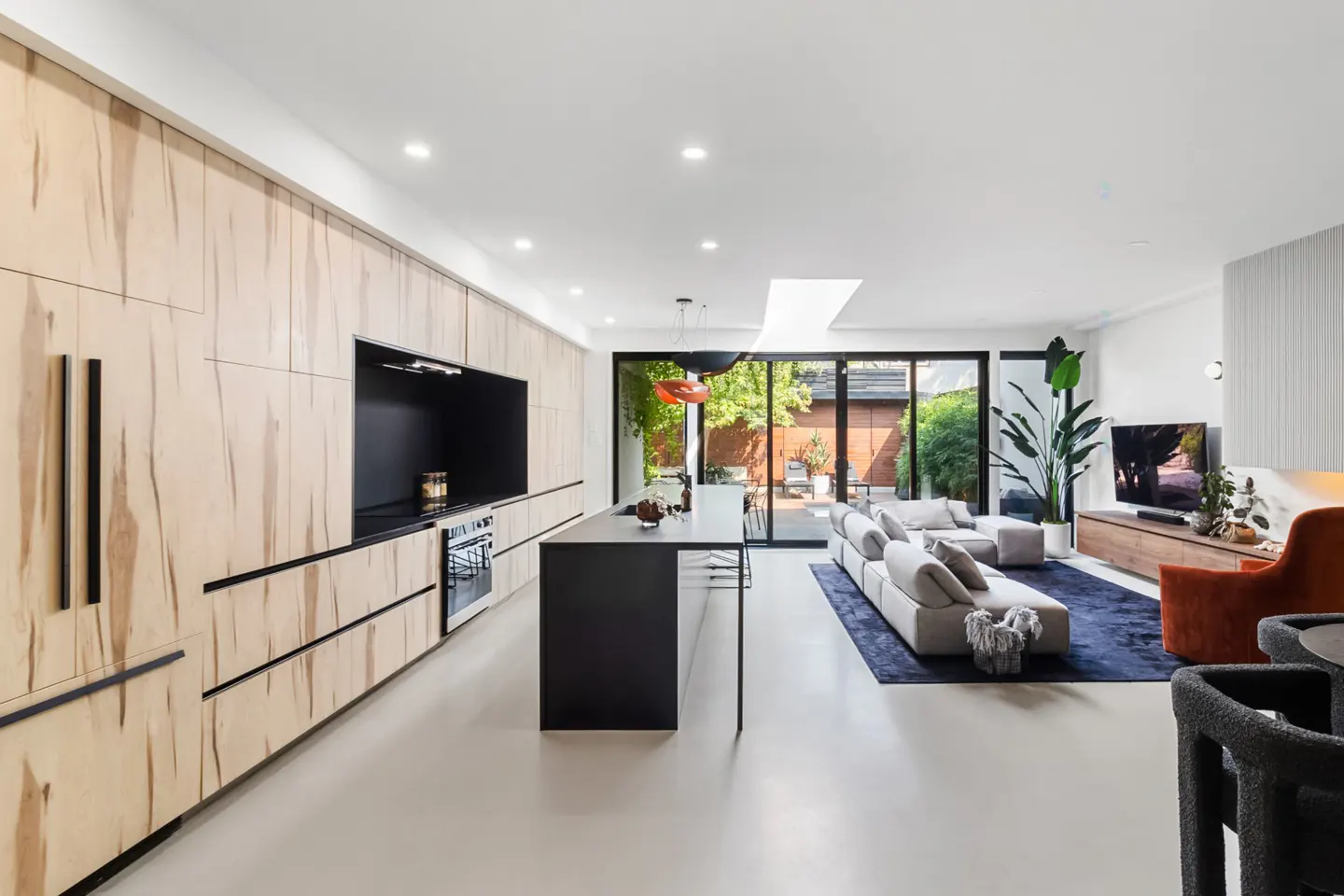 Open-concept kitchen and living room with wood cabinets, black island, gray sofa, and sliding glass doors to a patio.