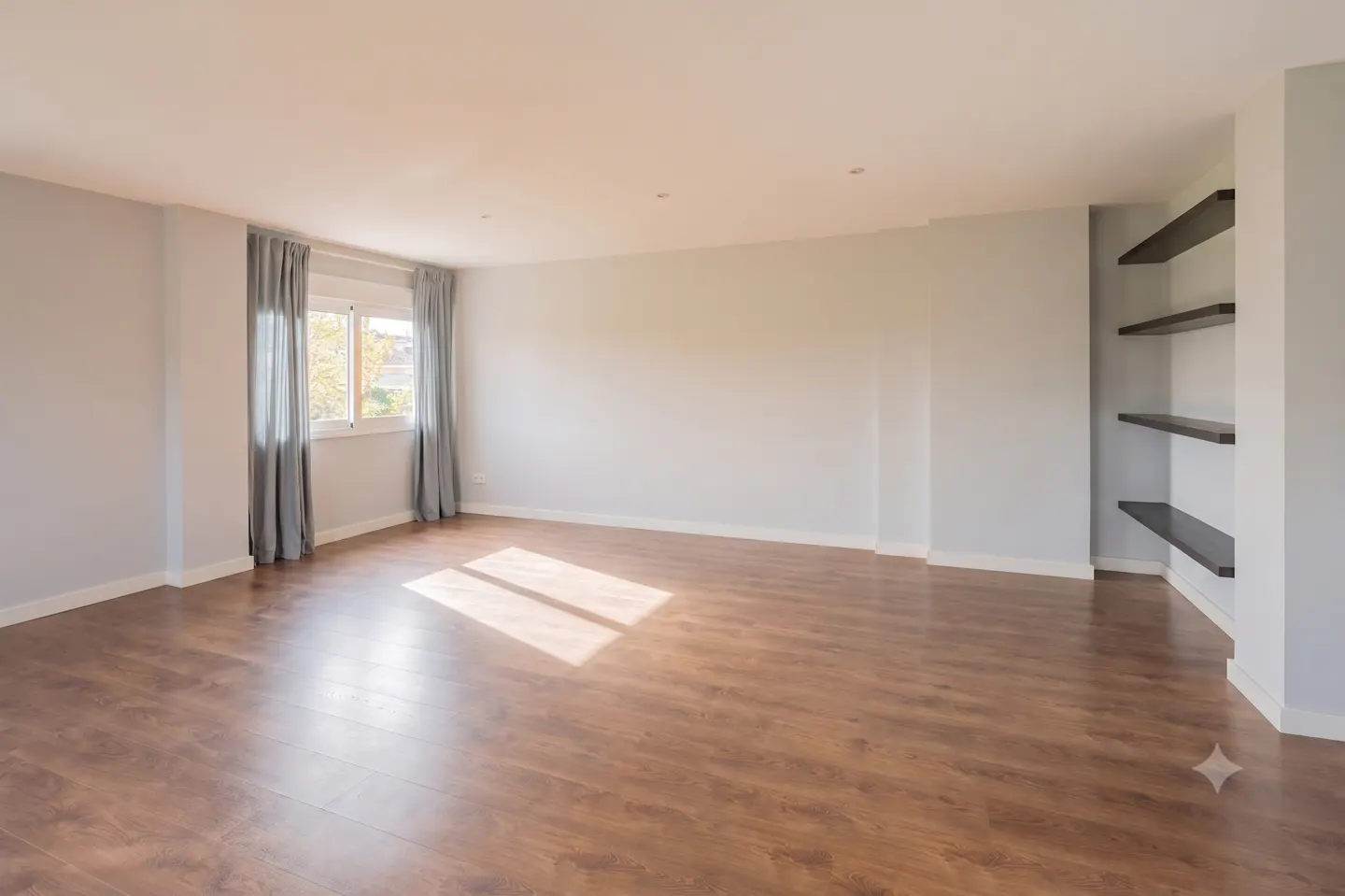 Empty living room with light gray walls, wood-look flooring, a window with gray curtains, and built-in dark wall shelves.