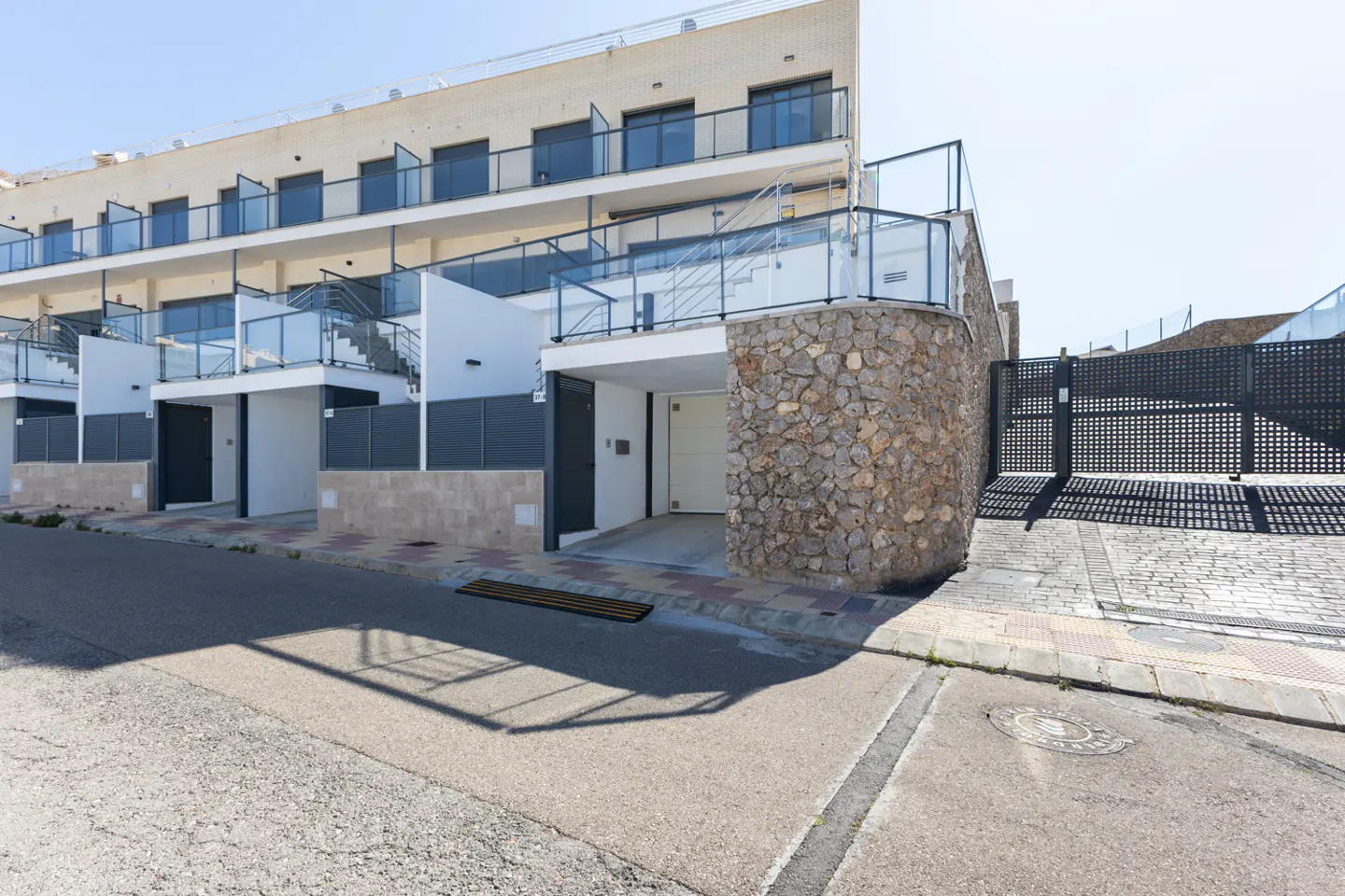 Exterior view of modern townhouses with white walls, glass balconies, and stone accents on a sunny day.