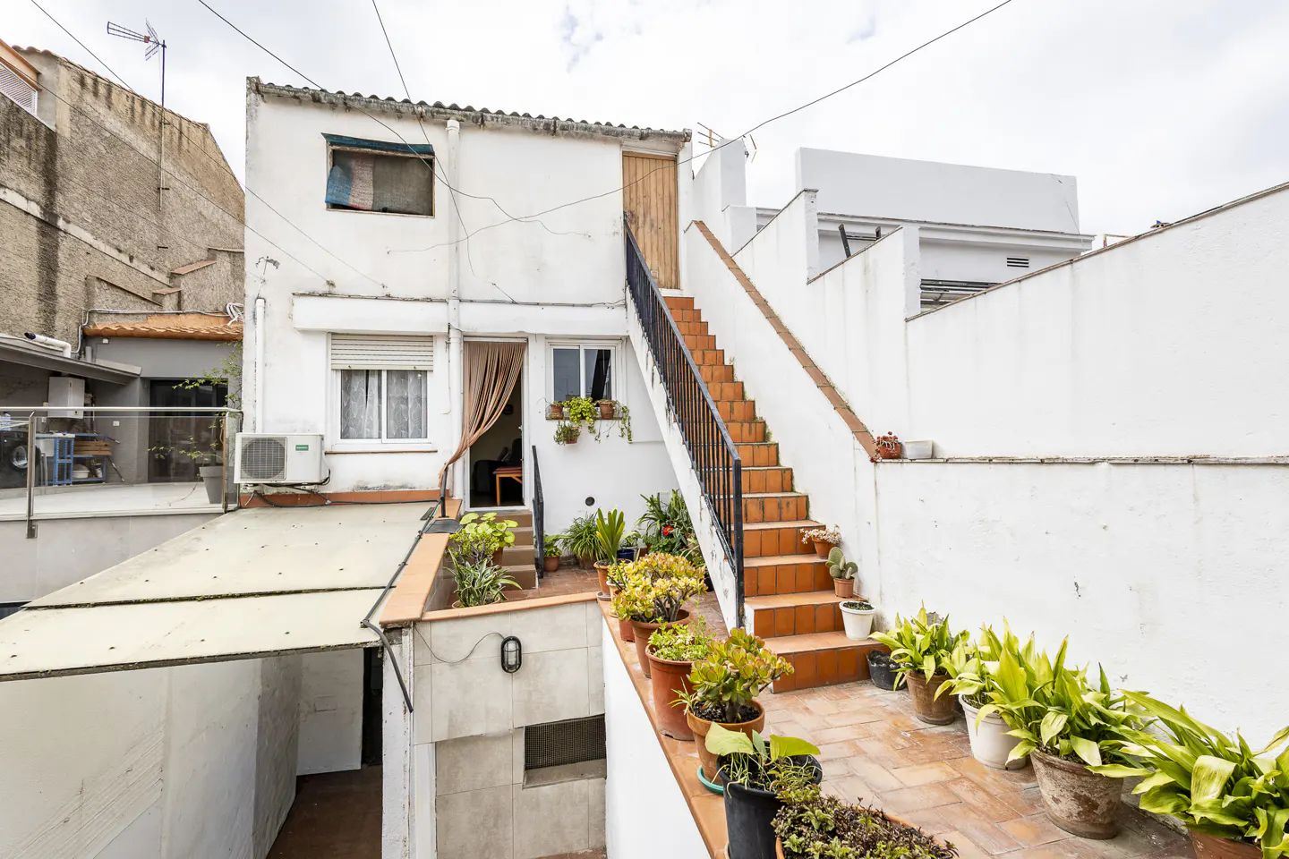 Exterior view of a white building with a brick staircase, potted plants, and a garage entrance.