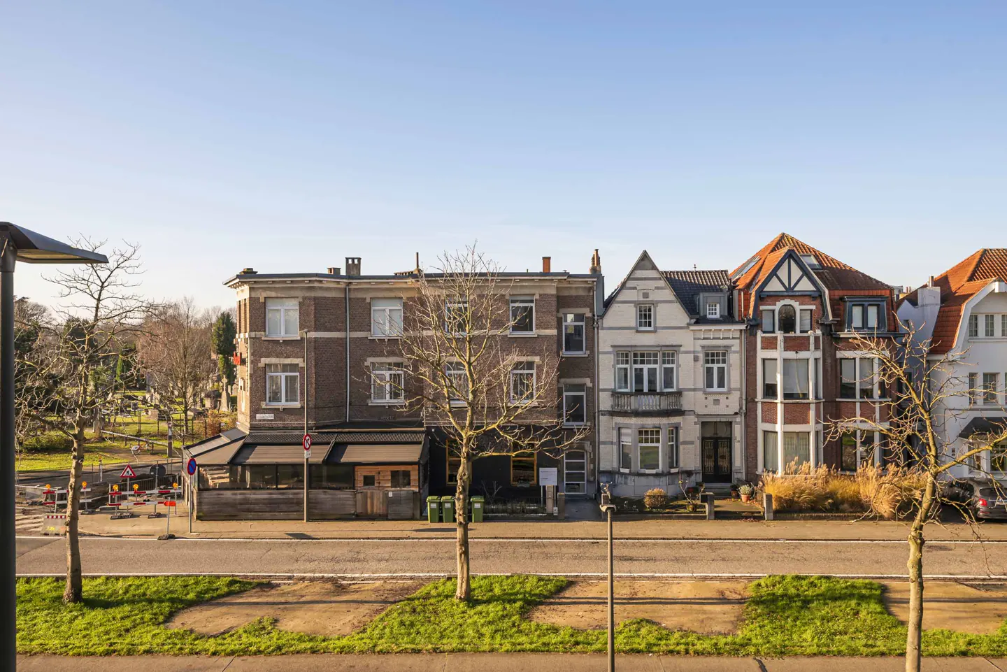 Row of multi-story townhouses with varied architectural styles and colors, street in front, blue sky.
