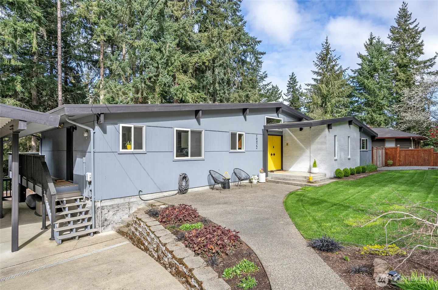 Exterior of a gray mid-century modern home with a bright yellow front door and a lush green lawn.