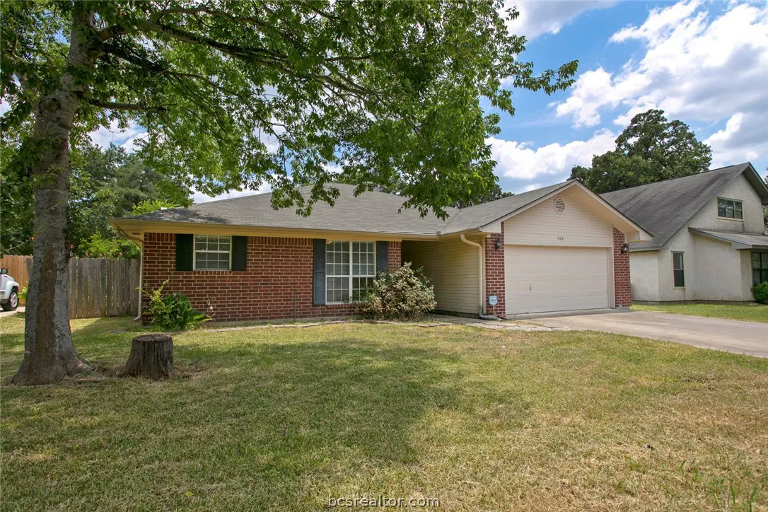 A single-story brick house with a two-car garage and a green lawn on a sunny day.