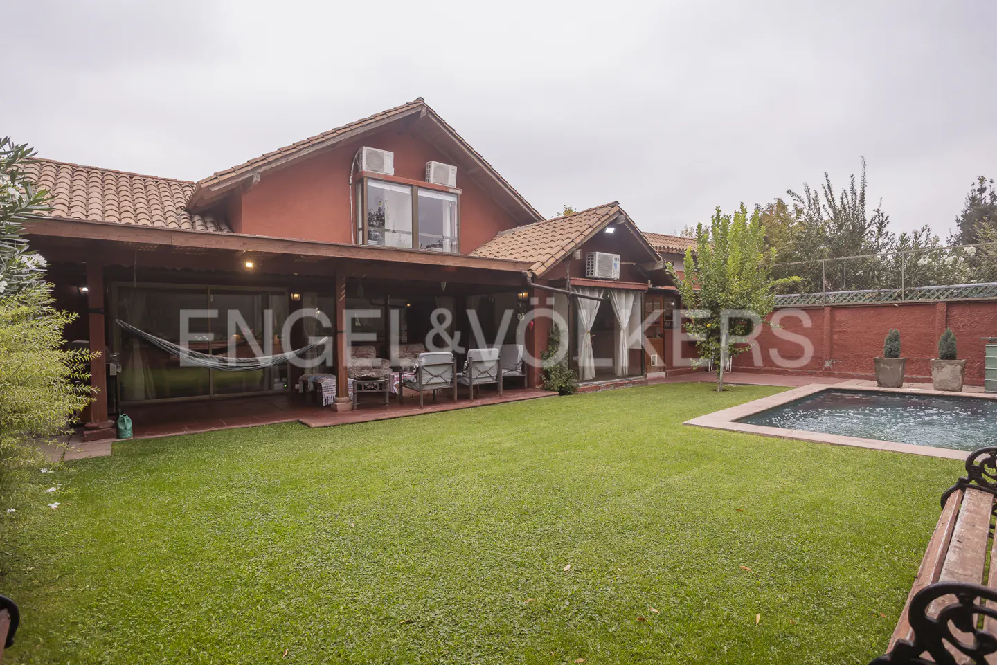 Exterior view of a red house with a pool and green lawn. A covered patio has a hammock and seating.