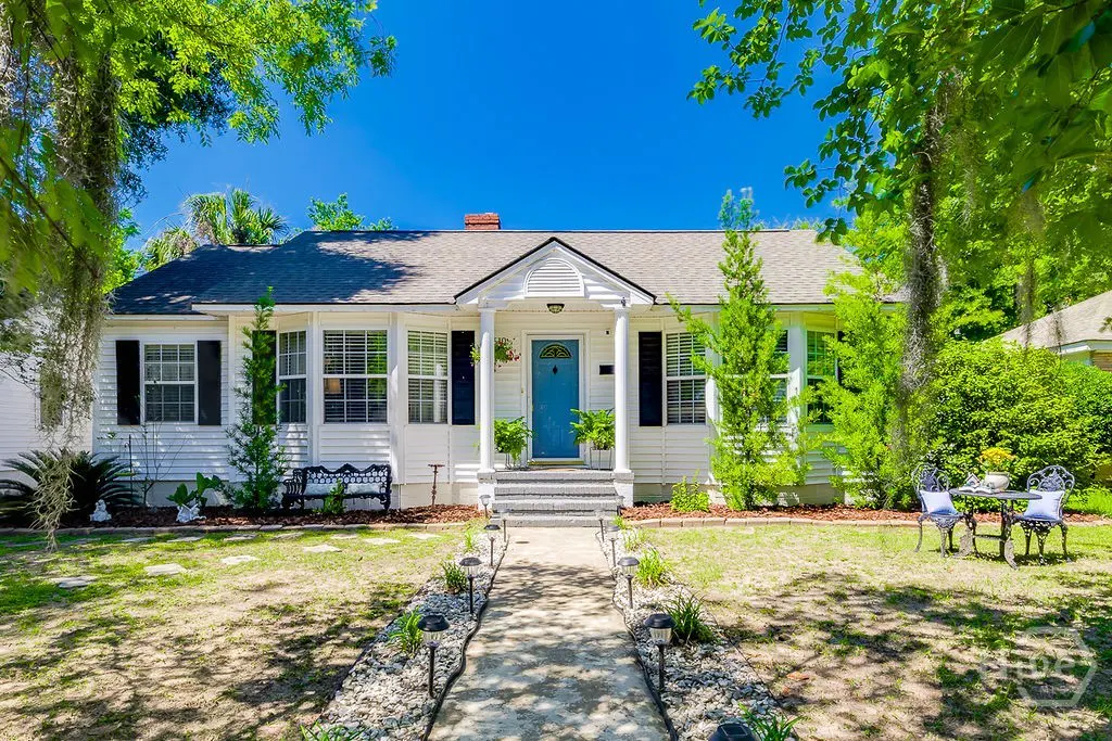 White cottage with a bright blue front door, black shutters, and a stone walkway leading to the porch under a blue sky.