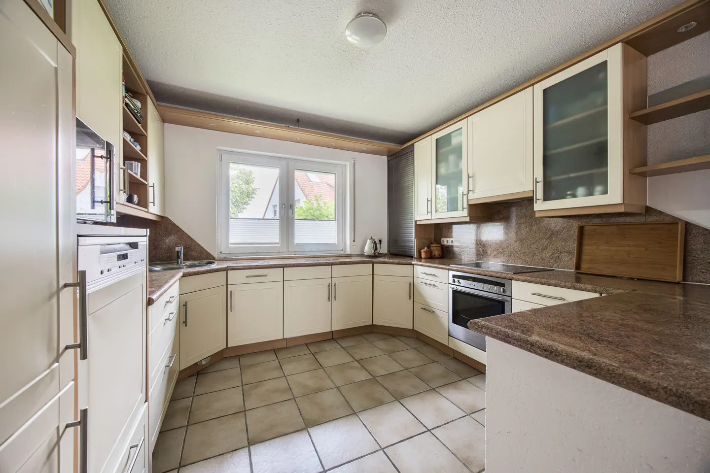 U-shaped kitchen with cream cabinets, brown granite countertops, tiled floors, and a window above the sink.