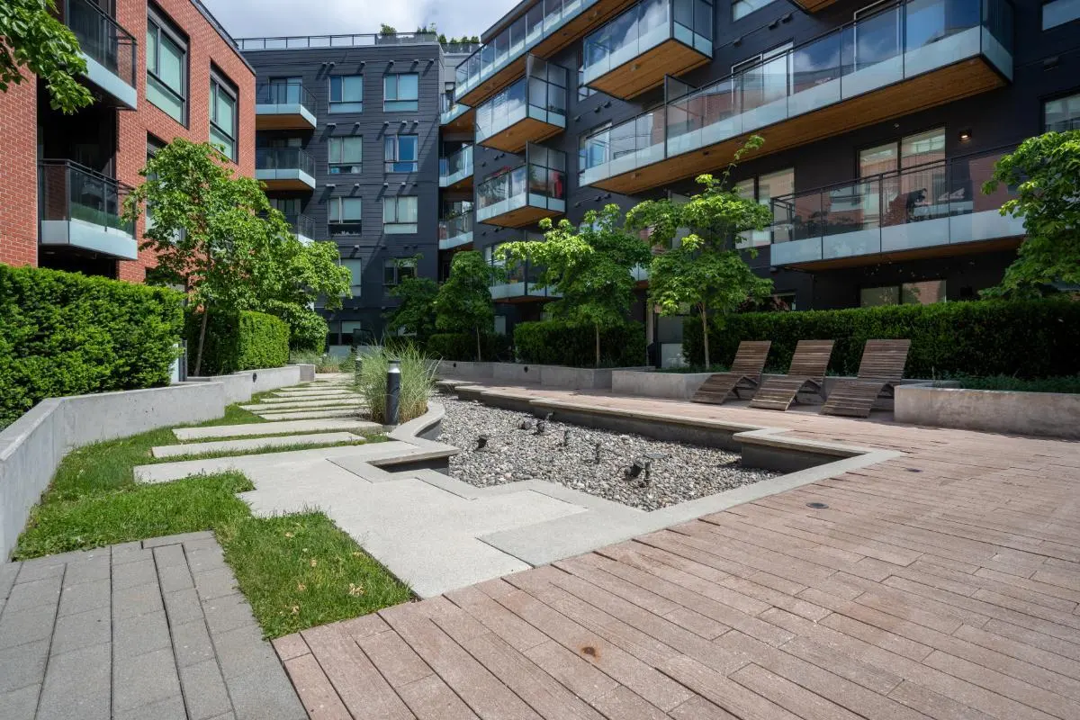 Condo courtyard with a water feature, lounge chairs, and green landscaping. Modern buildings with balconies are in the background.