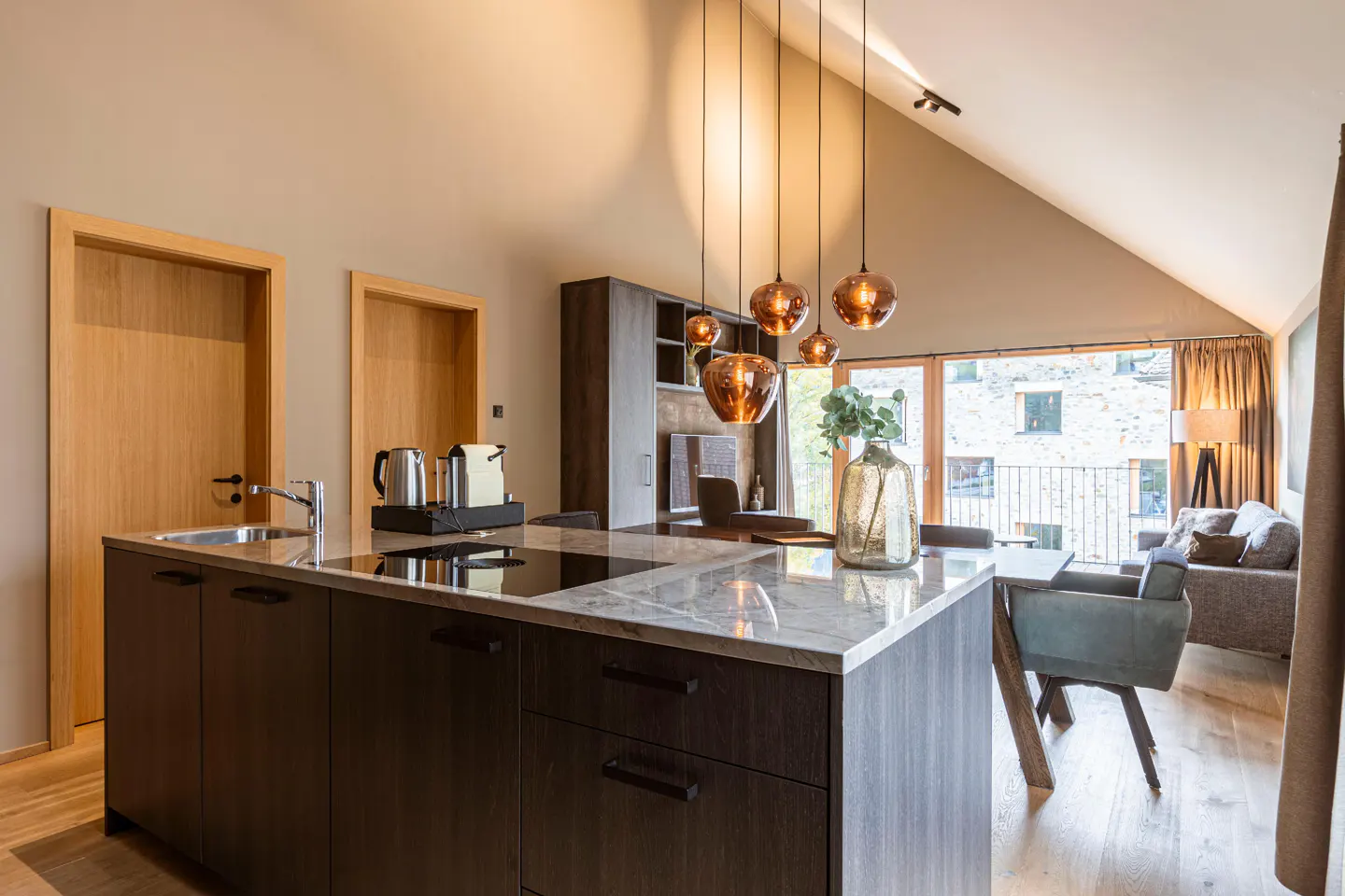 Modern kitchen island with marble countertop, dark cabinets, and hanging glass pendant lights in an open-plan living space.
