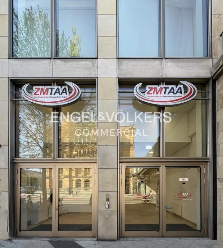 Exterior of Engel & Völkers Commercial office with glass doors and windows. "Z MTAA" sign above entrance. Building is stone.