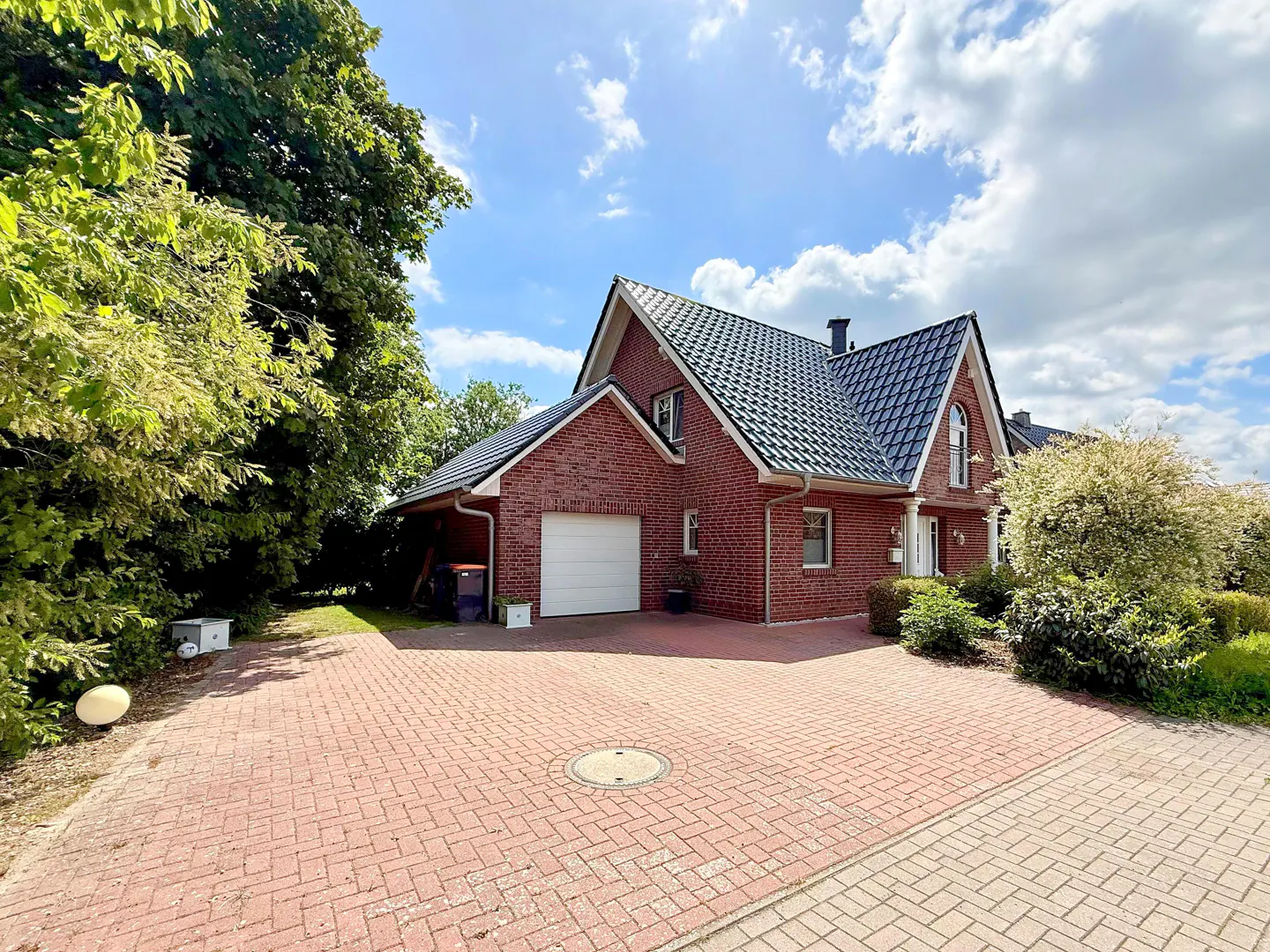 Red brick house with a dark roof, white garage door, and brick driveway on a sunny day.