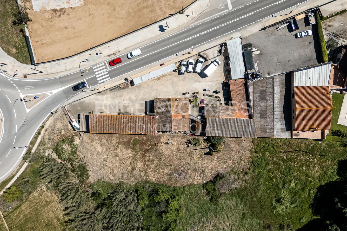 Aerial view of an Engel & Volkers commercial property with a brown roof, near a road with cars and a roundabout.