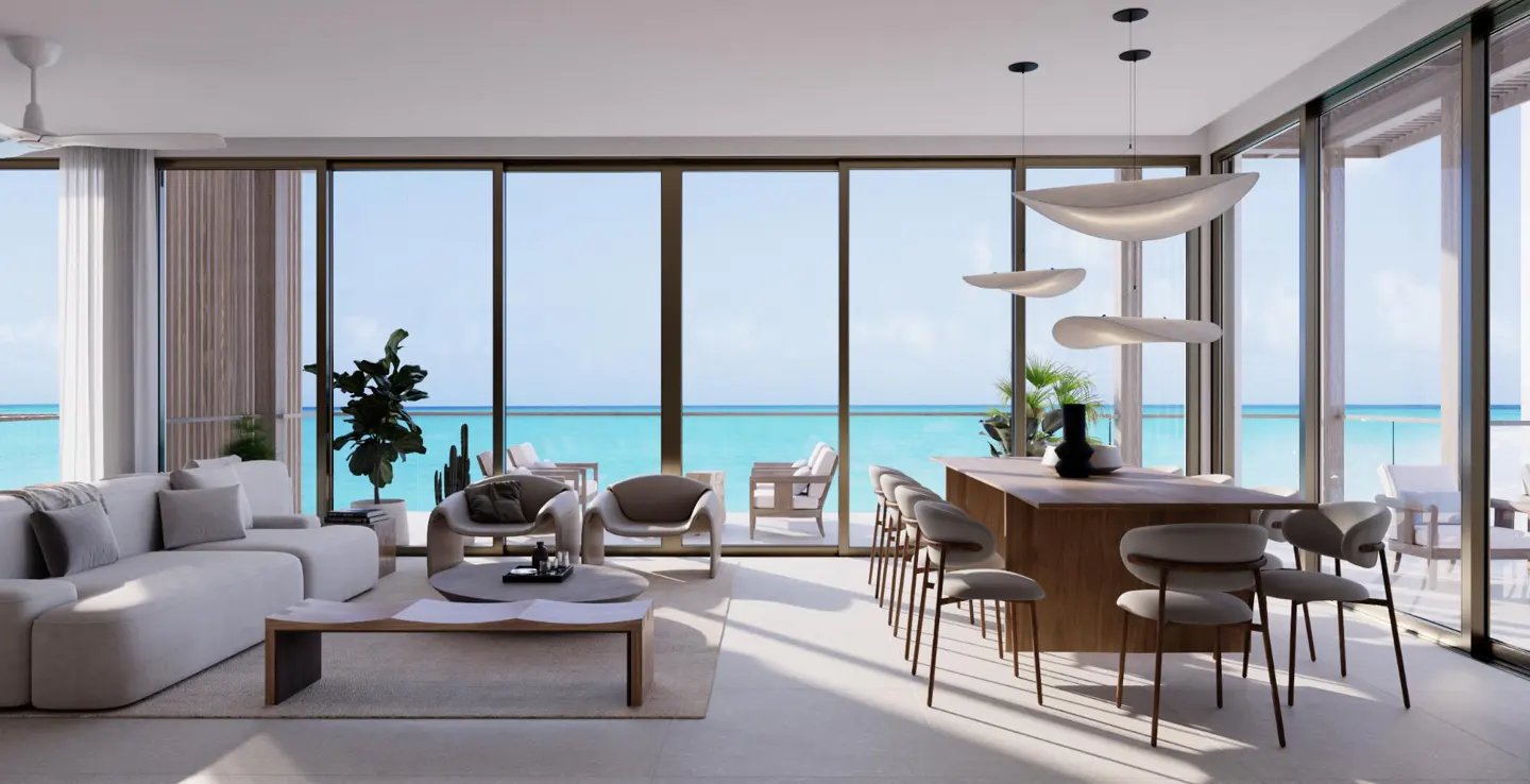Bright, modern living room with ocean view. Beige sofa, chairs, wood table, and island with seating. Large windows frame turquoise water.