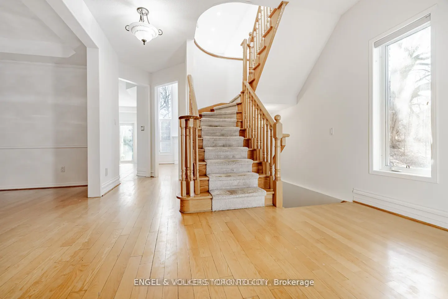 Bright foyer with hardwood floors, white walls, and a carpeted staircase with wooden banister. A window lets in natural light.