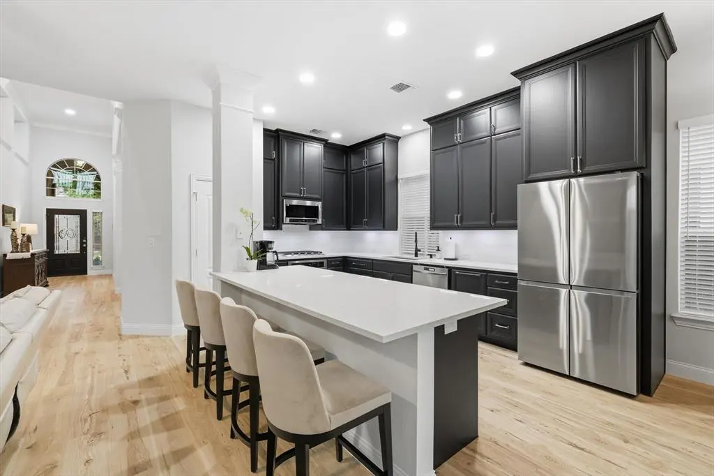 A modern kitchen with black cabinets, stainless steel appliances, and a white countertop island with four beige bar stools.