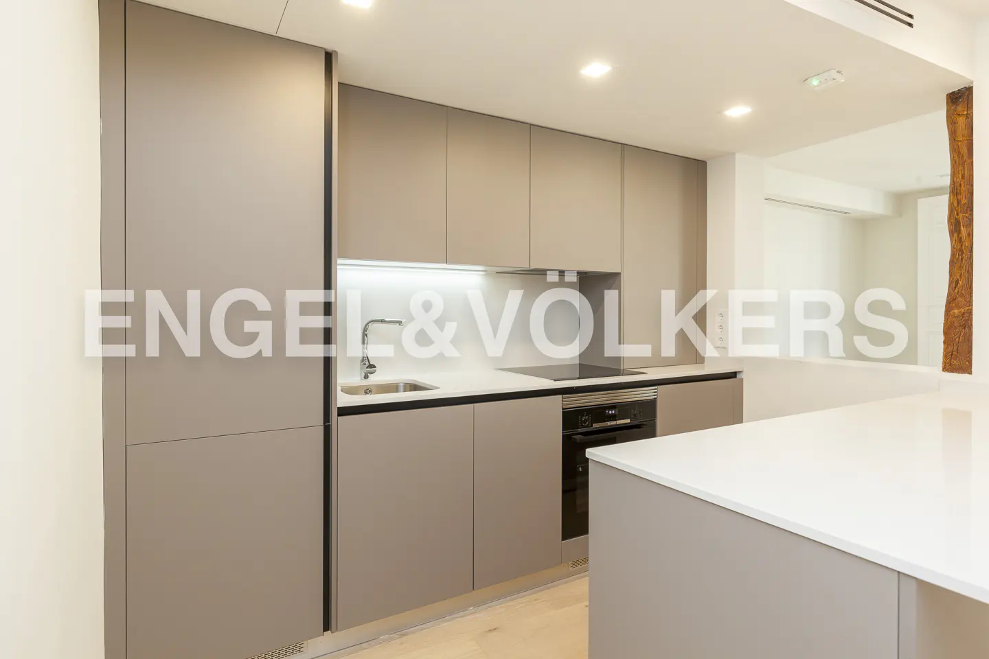 Modern kitchen with matte taupe cabinets, white countertops, built-in oven, and a white kitchen island.