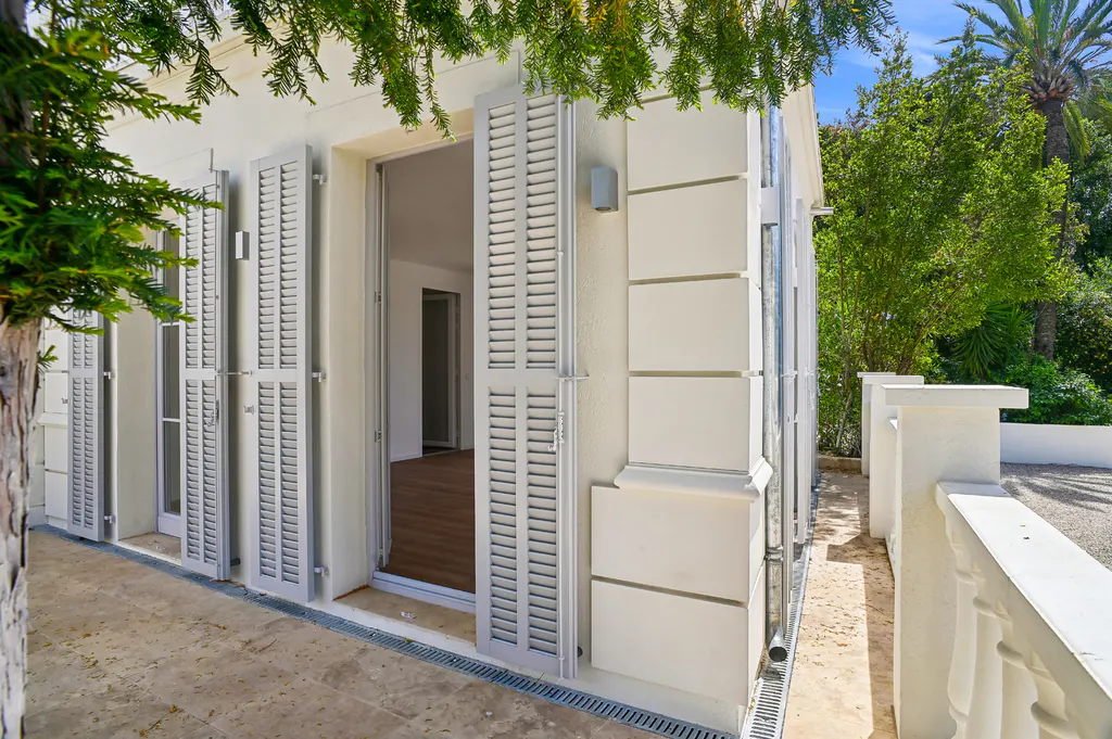 Exterior view of a white building with open gray shutters and an open door, revealing a glimpse of the interior.