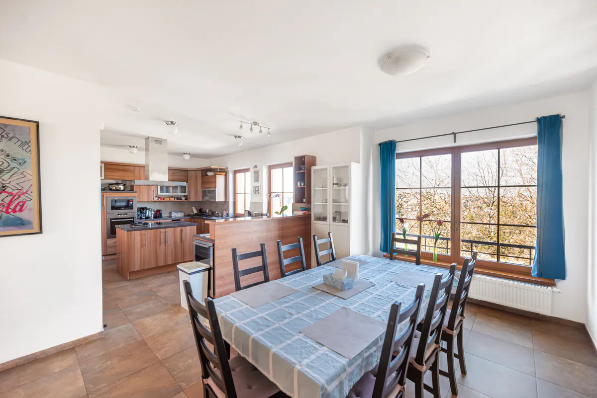 Open-concept kitchen and dining area with a large table, blue tablecloth, and a window with blue curtains.