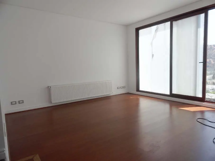 Empty room with white walls, wood floors, and a large window with white curtains. A white radiator is on the wall.